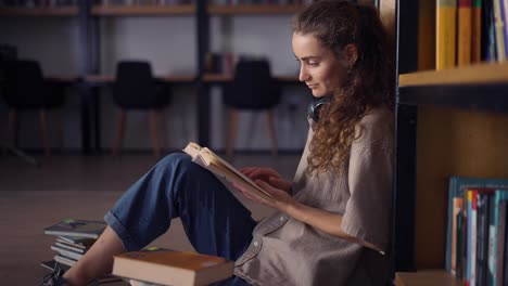 student in headphones sitting against bookshelf with a books on the floor, close up