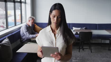 Mixed-race-businesswoman-standing-using-digital-tablet-in-modern-office