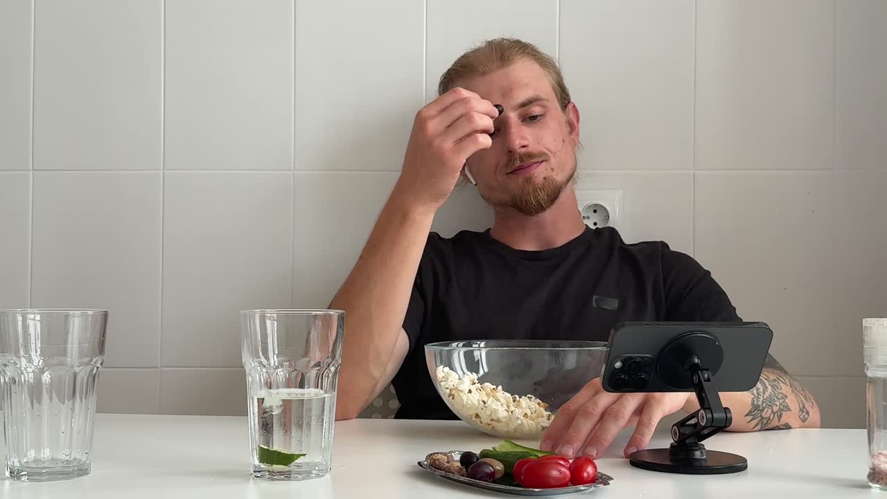 Молодой человек ест попкорн и закуски, глядя в телефон.