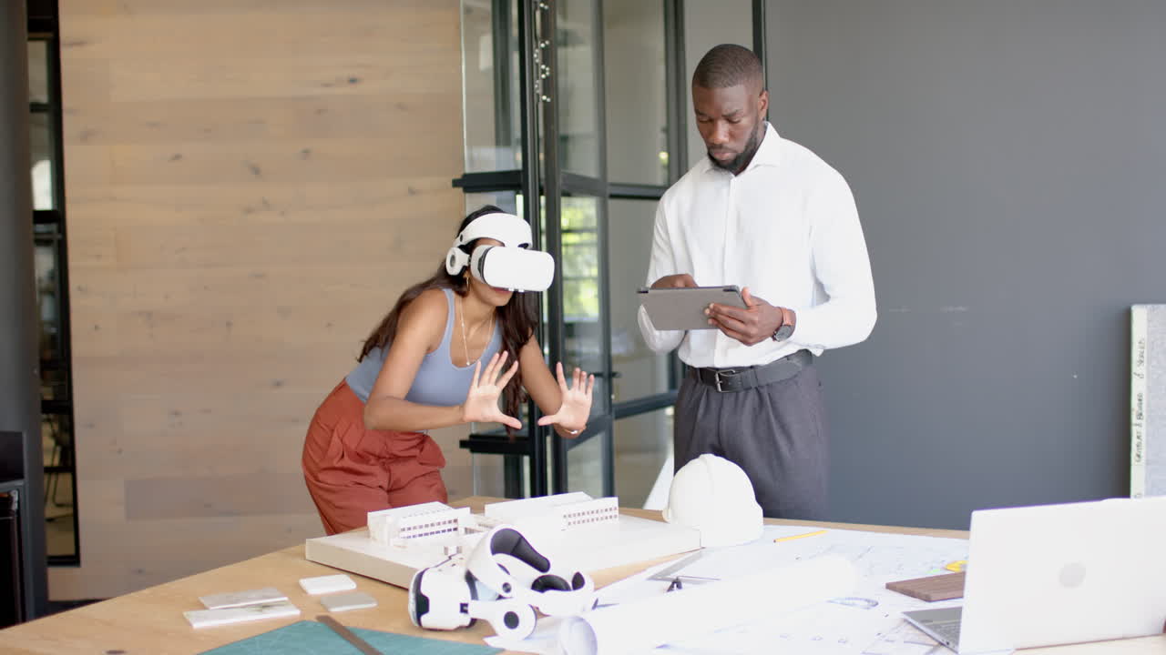Using VR headset, woman interacting with virtual model while man reviews tablet
