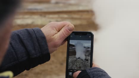 Touristen-Stehen-In-Der-Nähe-Der-Dampfentlüftung-Und-Halten-Ein-Telefon-In-Der-Hand-Und-Machen-Ein-Foto,-Island