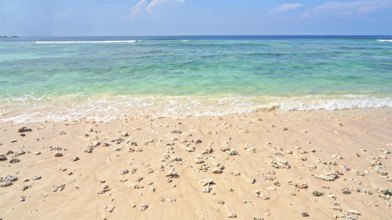 부서진 산호 조각이 배경에 맑은 청록색 물로 해변을 덮고 있습니다.