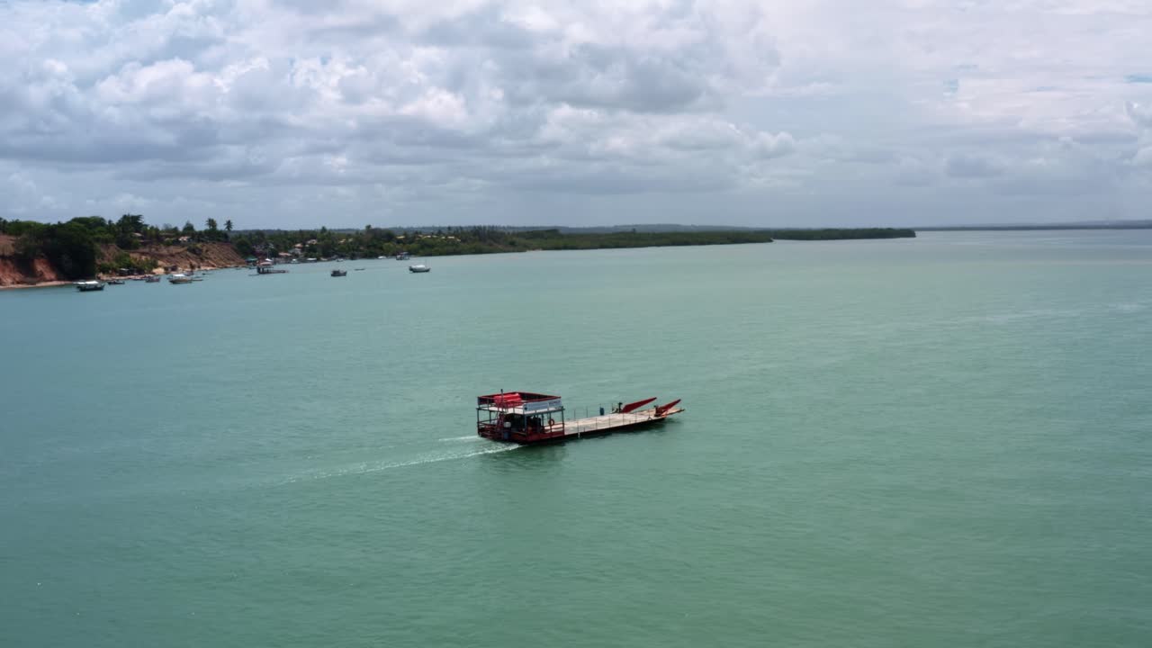 Aerial drone shot rotating around a large red ferry transport boat carrying a car across the Malemb&aacute; crossing of the Guara&iacute;ras Lagoon in Tibau do Sul near Pipa, Brazil in Rio Grande do Norte
