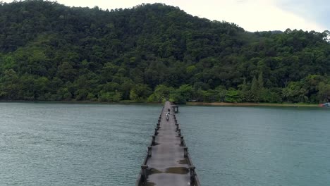 drone following 2 tourist on a scooter driving on a concrete pier on a tropical island cropped