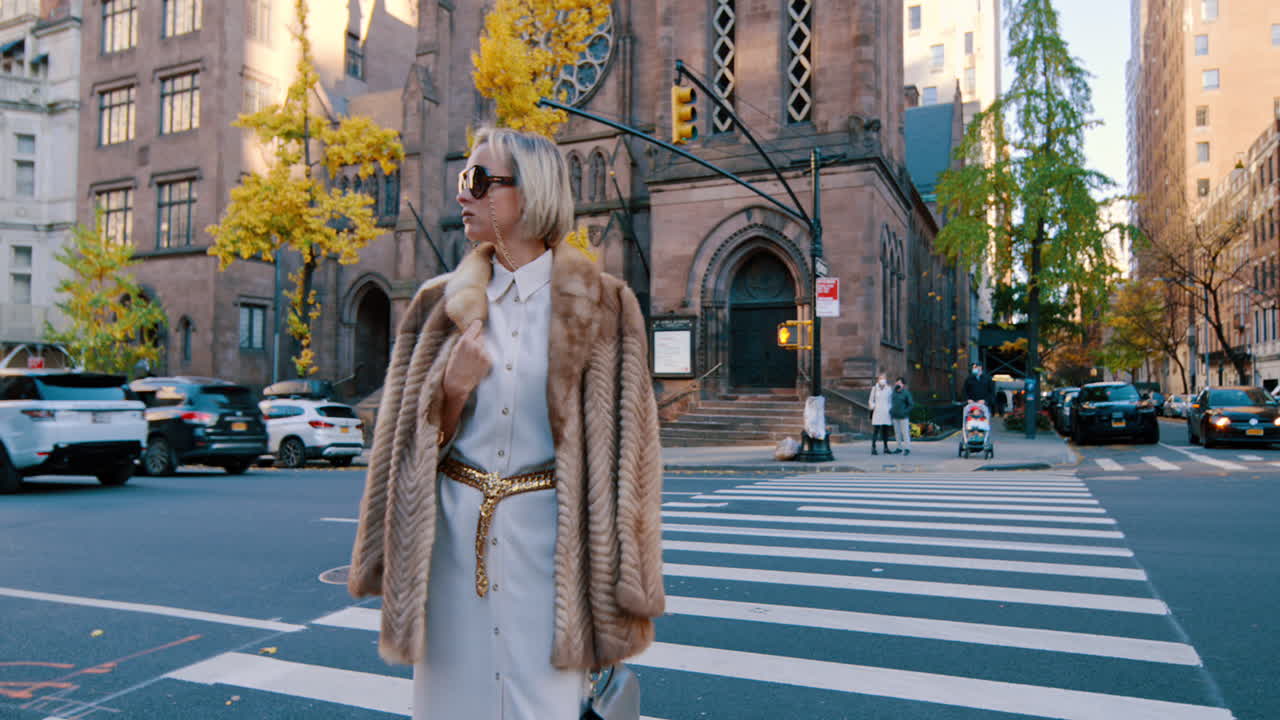 New York, USA, 25 October 2025: Fashionable woman in fur coat walking on New York crosswalk. Woman wearing sunglasses and faux fur coat crossing urban street with historic church in background