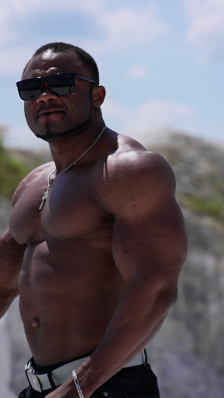 Waist up portrait view of the athletic naked man wearing glasses walking outside and showing his naked torso. Man posing at the sandy beach. Vertical video
