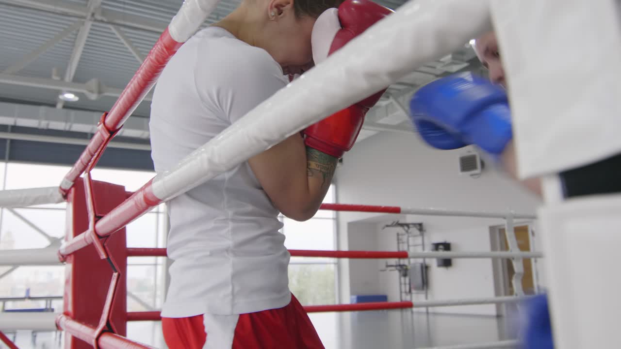 여자 권투 선수 가 권투 링 에서 로프 에 맞대는 상대 를 때리고 있다