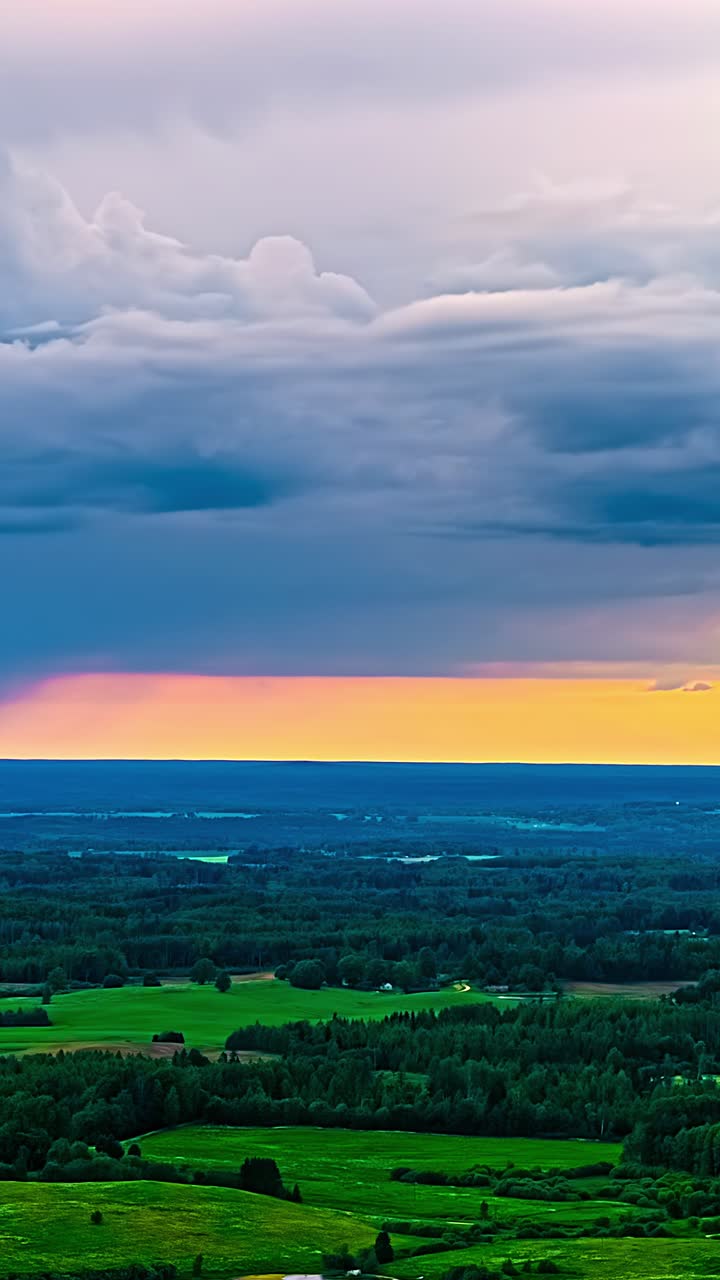 Aerial timelapse of layered storm clouds stretching across the sky over expansive forests and fields, with warm sunset tones glowing beneath the cloud deck, vertical