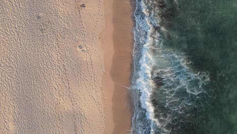 4k fly out of waves and sand coast in beautiful turquoise sea texture background top view aerial