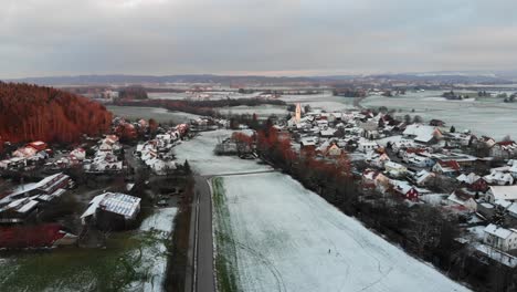 Drohnenflug-über-Ein-Verschneites-Dorf-Mit-Einer-Stark-Befahrenen-Straße-In-Der-Nähe