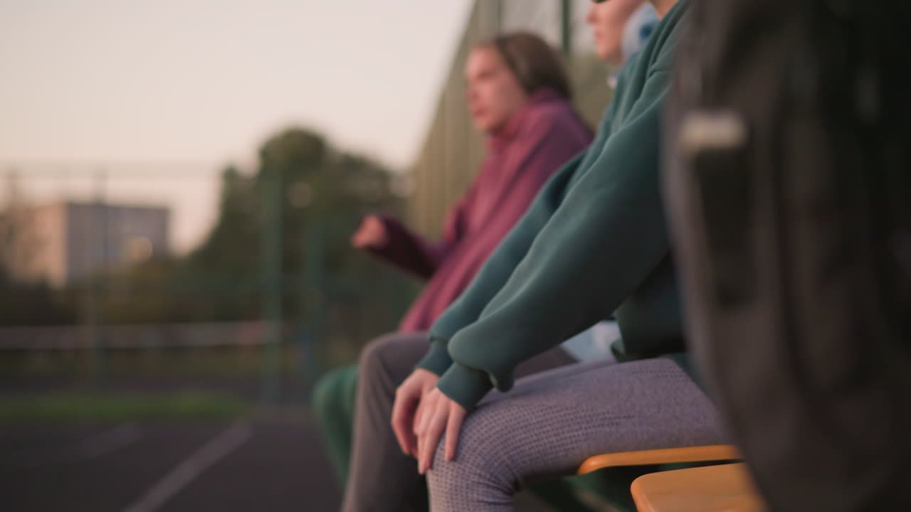 vista lateral de atletas relajándose después de una larga sesión de entrenamiento con una dama de verde bajando la cabeza mientras descansa, reflejando un momento de recuperación y relajación después de un ejercicio intenso