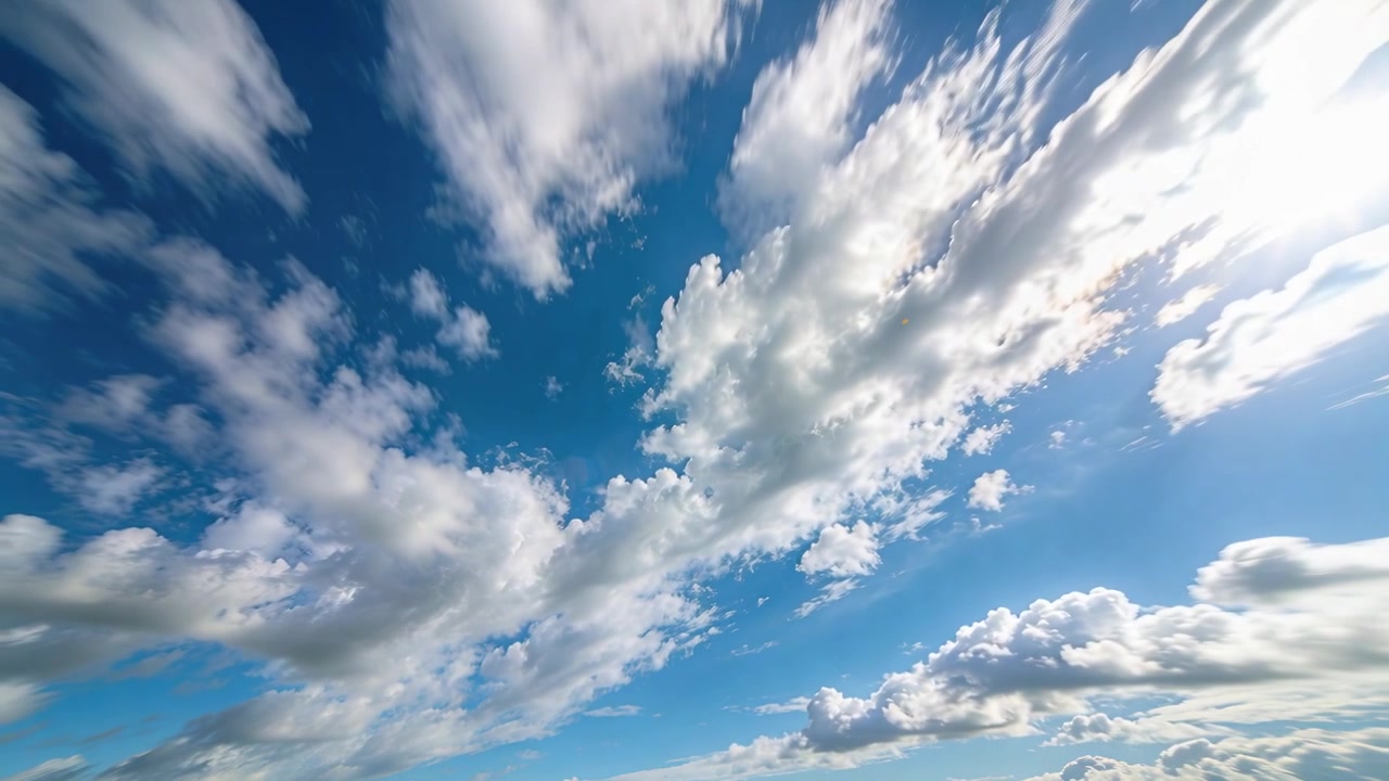 Una banda di nuvole cumulo si sposta e si assottiglia mentre la telecamera si inclina verso l'alto, rivelando un bagliore solare nel cielo blu.