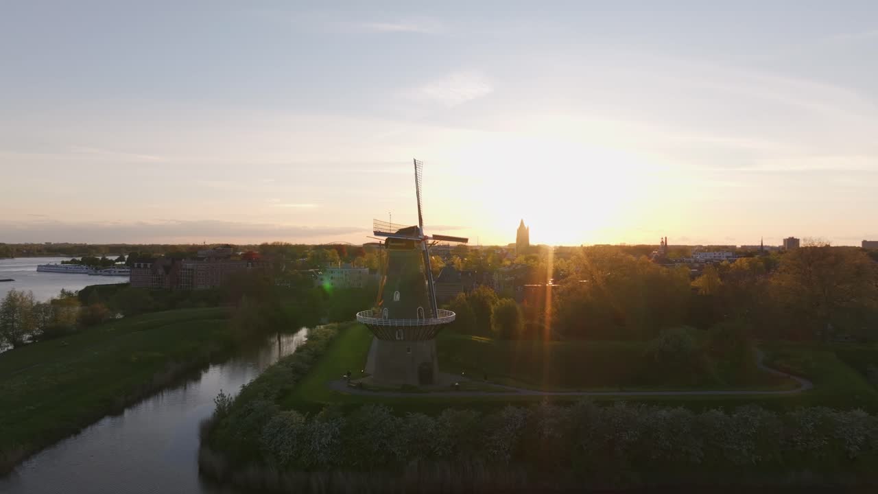Gorinchem, Hollanda'da nehir kenarındaki patika ve ağaçların üzerinde alacakaranlıkta yel değirmeni