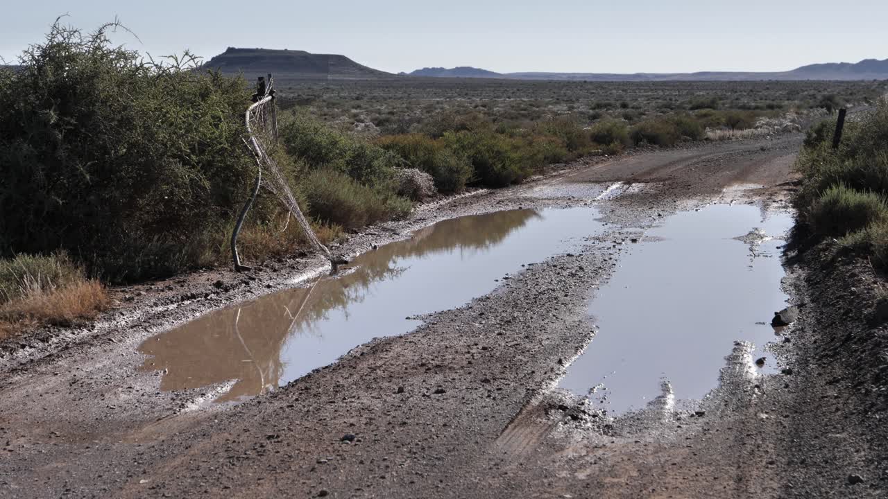 disparo estático: charcos de barro en la puerta de la valla rota en un paisaje plano y árido