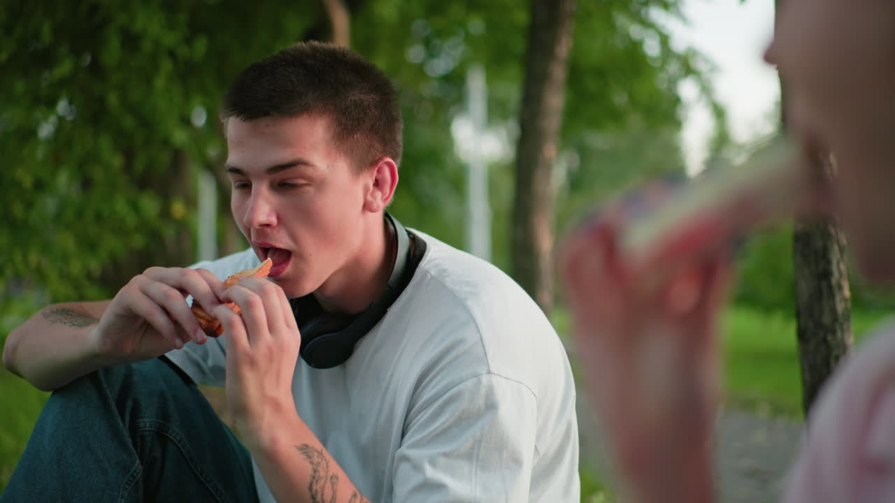 primer plano de una mujer haciendo un brindis con pan, un hombre sosteniendo pan en el fondo, creando una atmósfera de picnic con vegetación y sol