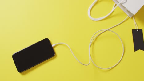 overhead view of smartphone and white gift bag with black sale tag on yellow background