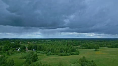 Ominosas-Nubes-Azul-Oscuro-Moviéndose-Lentamente-Sobre-Exuberantes-Campos-Verdes-Con-árboles-Debajo-En-Un-Paisaje-Dramático