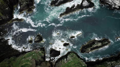 Aerial-top-down-view-4k-footage-by-drone-of-ocean-blue-waves-break-on-high-cliff-of-a-rocky-mountain