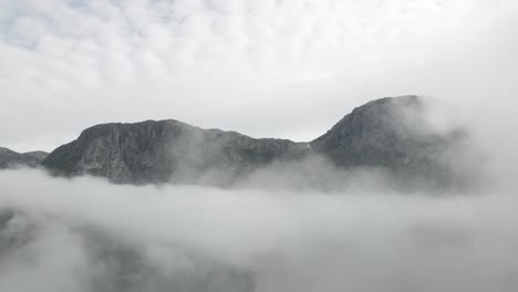 Rocky-mountain-peeks-standing-above-fluffy-clouds,-aerial-view