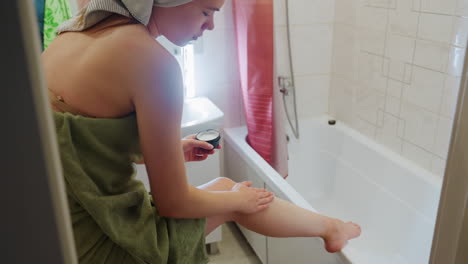 young girl standing in bathroom wrapped in towel, placing one leg on sink, applying cream, with mirror reflection and light, part of skincare routine, moisturizing, self-care moment