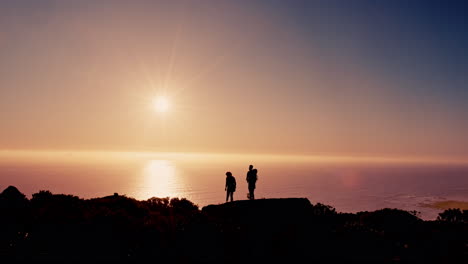 silhouette of a couple standing on a cliff at sunset overlooking the ocean