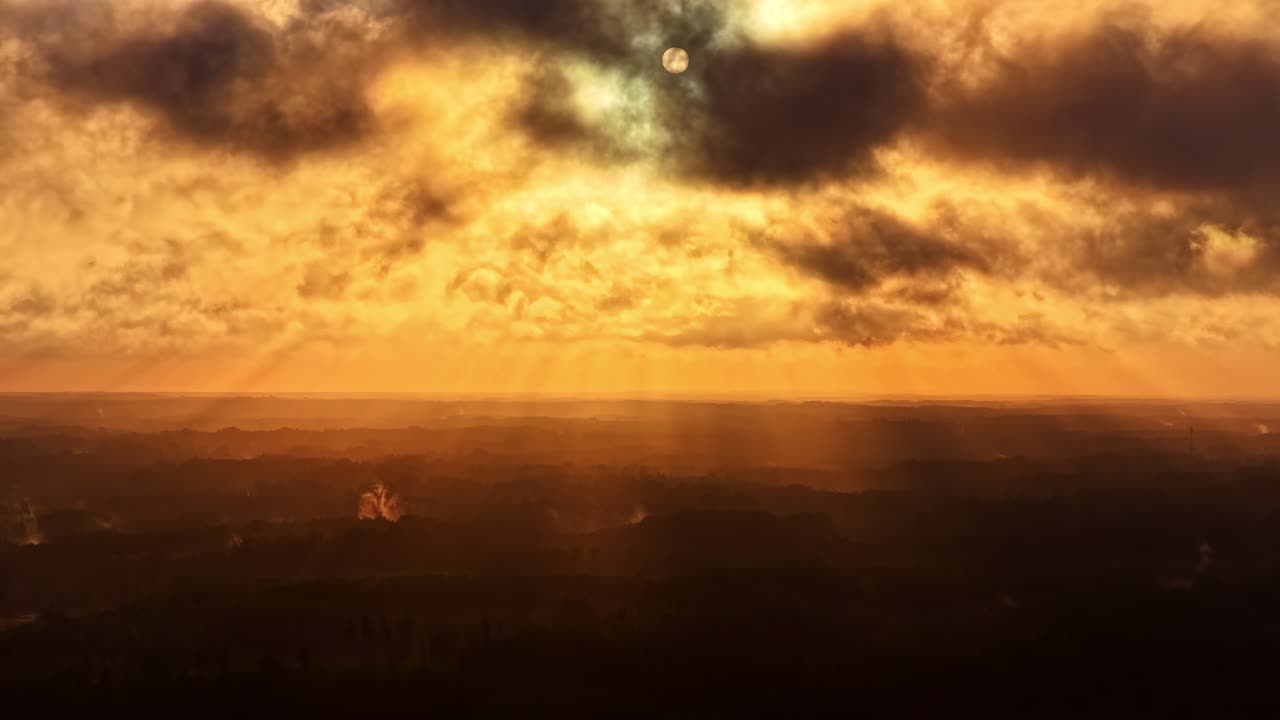 Dramatischer Zeitraffer der goldenen Stunde, in dem sich Wolken über den Himmel bewegen, während Sonnenstrahlen durchbrechen und ein intensives atmosphärisches Licht über einer dunklen Landschaft erzeugen