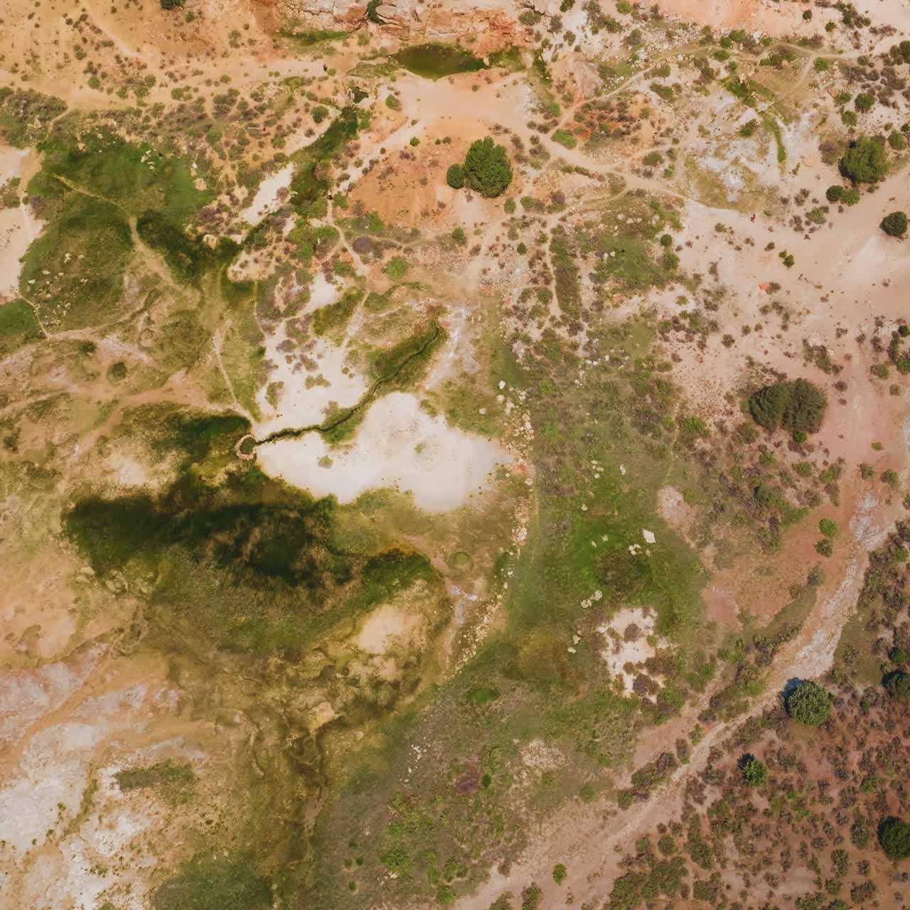 Descending to a dry land of Travertine Hot Springs in California, USA. Scarce greenery growing on the lifeless landscape. Top view