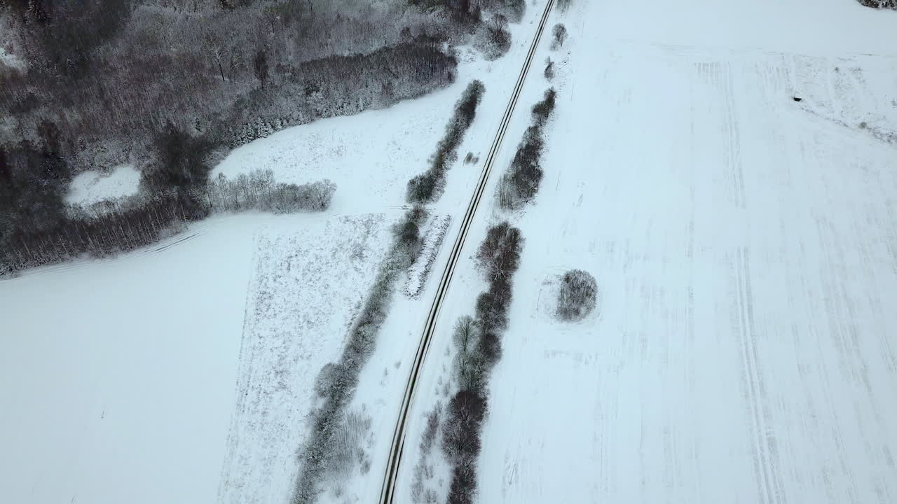 Drone footage of empty countryside road, besides snow covered forest, REVEALINGa view of near village - TILT UP in the end