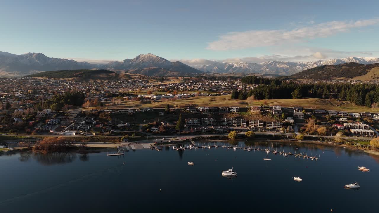 Beautiful 4K 60fps aerial shot of a small marina with boats moored in calm water at sunset. This peaceful scene on Lake Wanaka is ideal for projects about leisure, travel, or retirement
