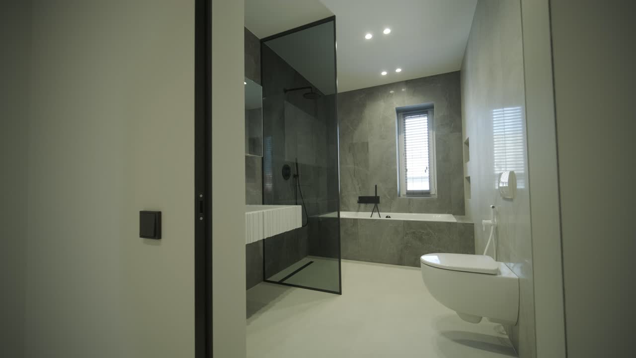 un baño elegante y moderno con una ducha cerrada con vidrio, un inodoro montado en la pared y elegantes azulejos de mármol.