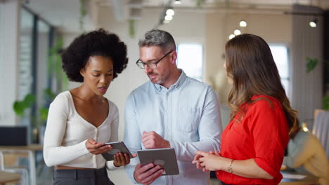 Multi-Cultural-Business-Team-With-Digital-Tablets-Meeting-In-Modern-Open-Plan-Office