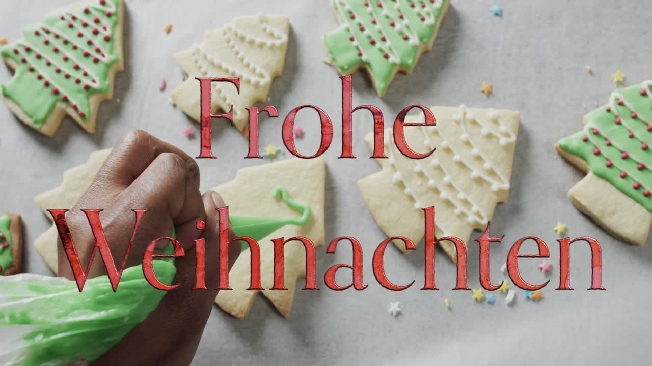 frohe weihnachten texto en rojo sobre la mano caucásica decorando galletas de navidad sobre fondo blanco