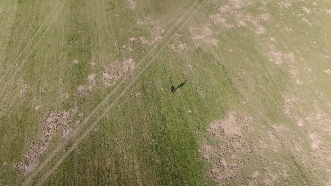 A man walking alone across a meadow, captured from a bird's-eye view in the evening light. Peaceful solitude in nature.