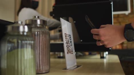 Close-up-of-female-hand-holding-smartphone,-scanning-qr-code-at-countertop