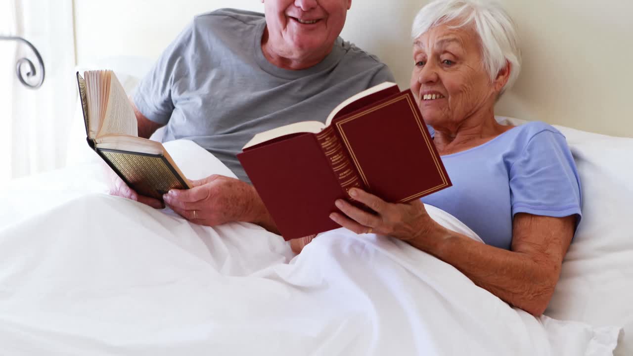 Casal idoso feliz lendo livro na cama