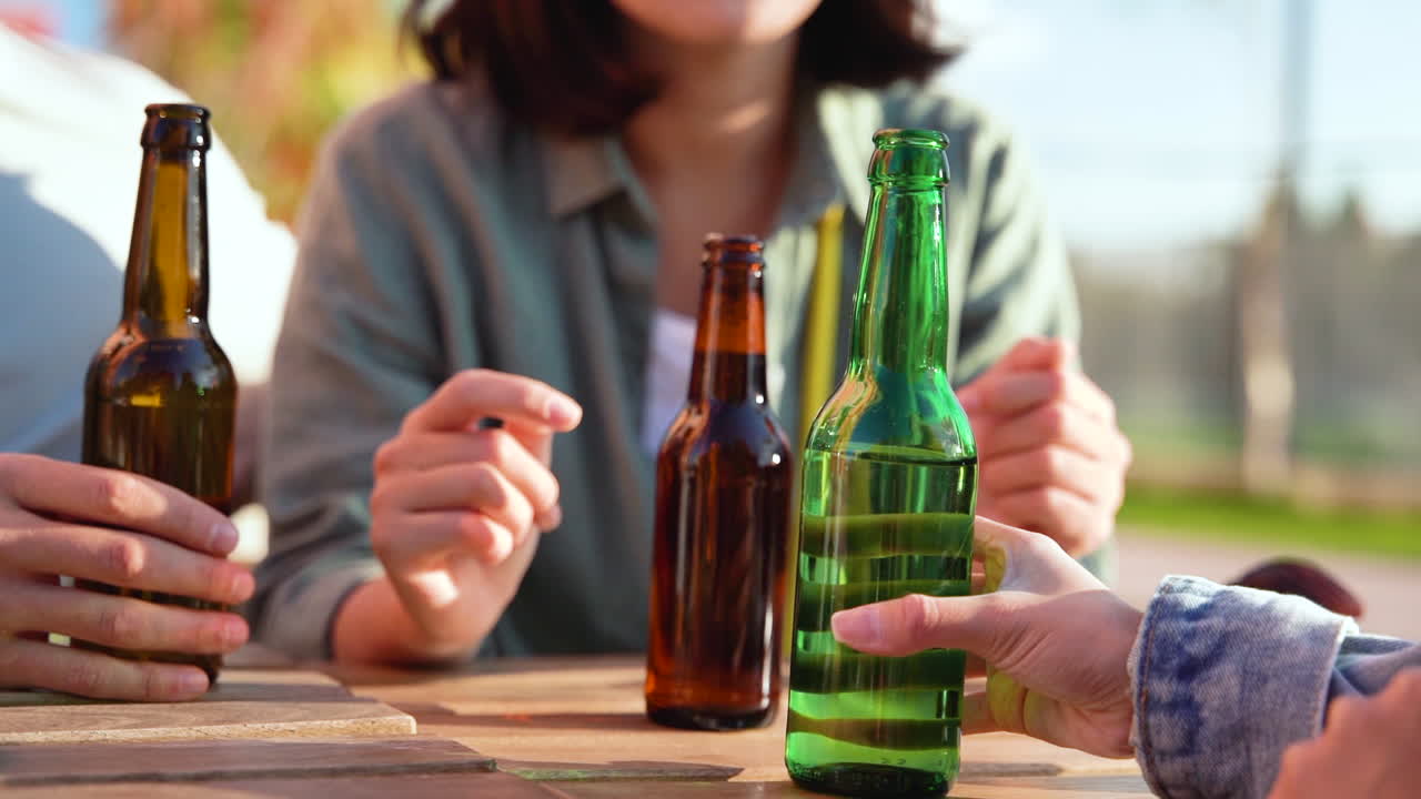 cerca de tres amigos irreconocibles hablando y bebiendo cerveza mientras se sientan a la mesa al aire libre en un día soleado