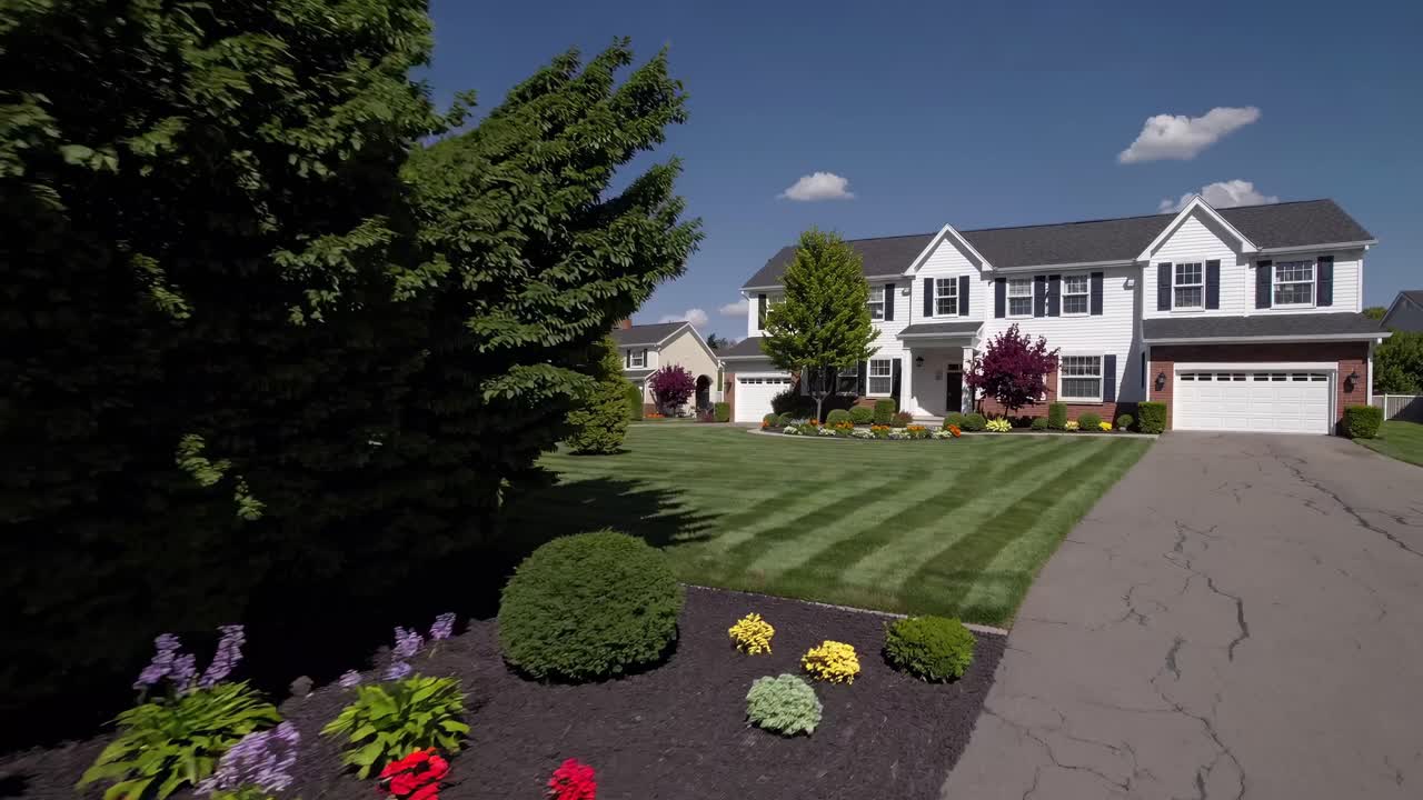 Aerial video captures a suburban home with a manicured lawn and vibrant landscaping