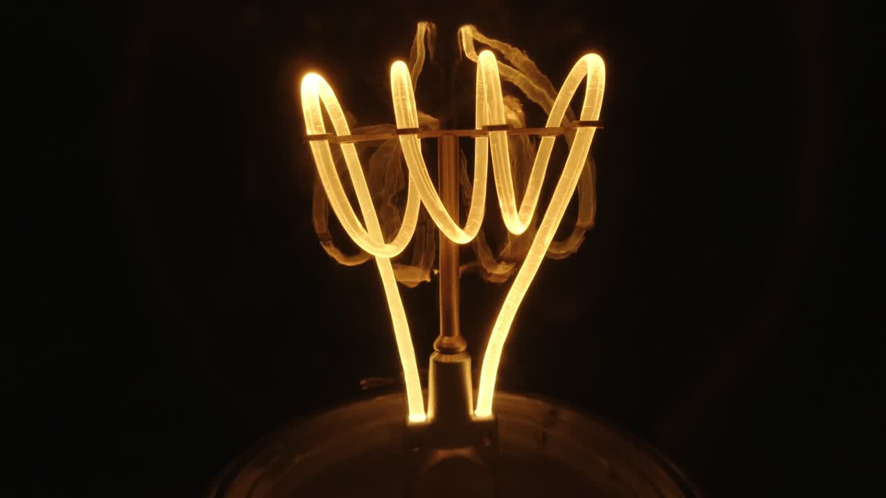 lámpara de bombilla de tungsteno parpadeante con una macro en espiral naranja. lámpara en espiral incandescente de primer plano en un fondo negro. bucle de video en bruto de 4k.