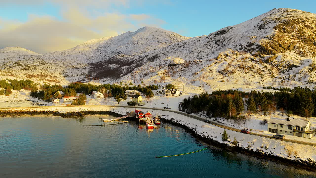 Et fantastisk filmatisk sveip over en snødekt norsk fiskerlandsby i Lofoten under den gylne timen, med tradisjonelle hytter og fjelltopper.