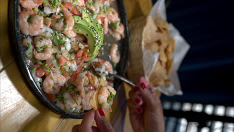 vertical slow motion of a woman preparing eating a tortilla chip with shrimp ceviche prepared with onion and tomato