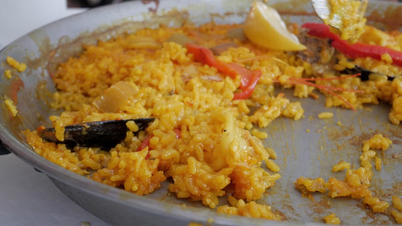 Close-up of a partially eaten seafood paella in a pan, with a spoon scooping rice
