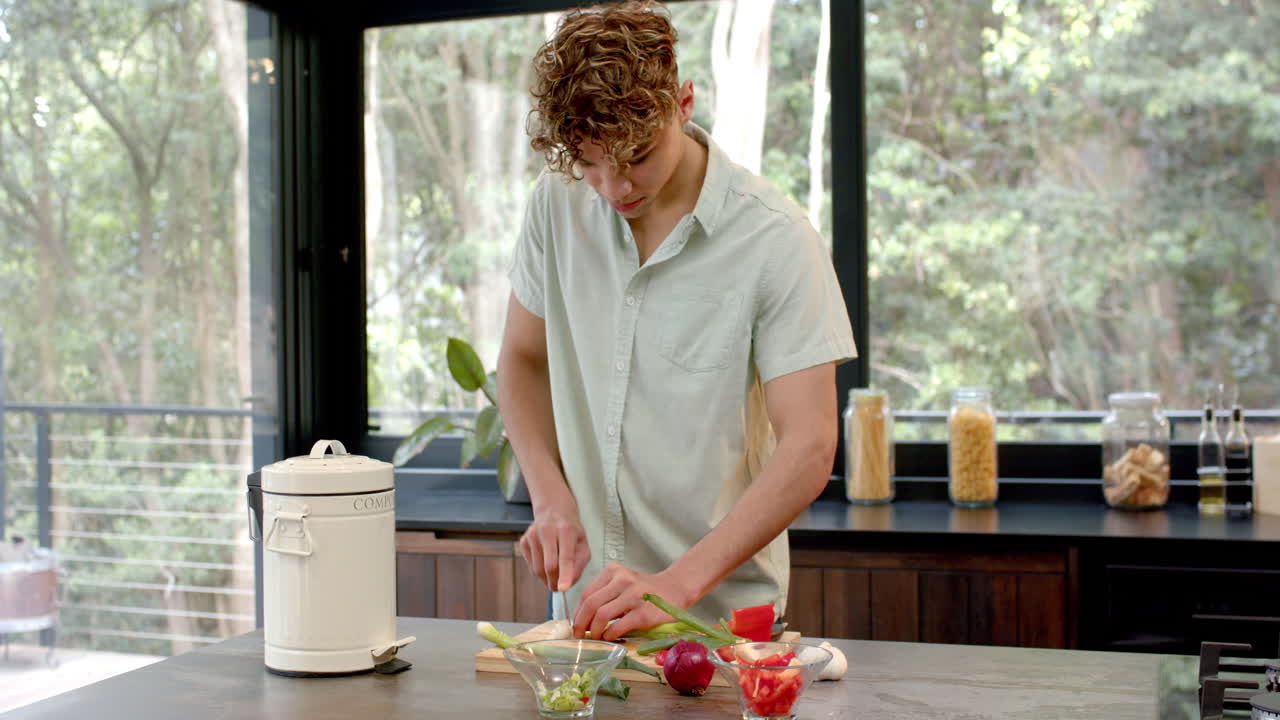 Young man chopping vegetables in modern kitchen with compost bin nearby