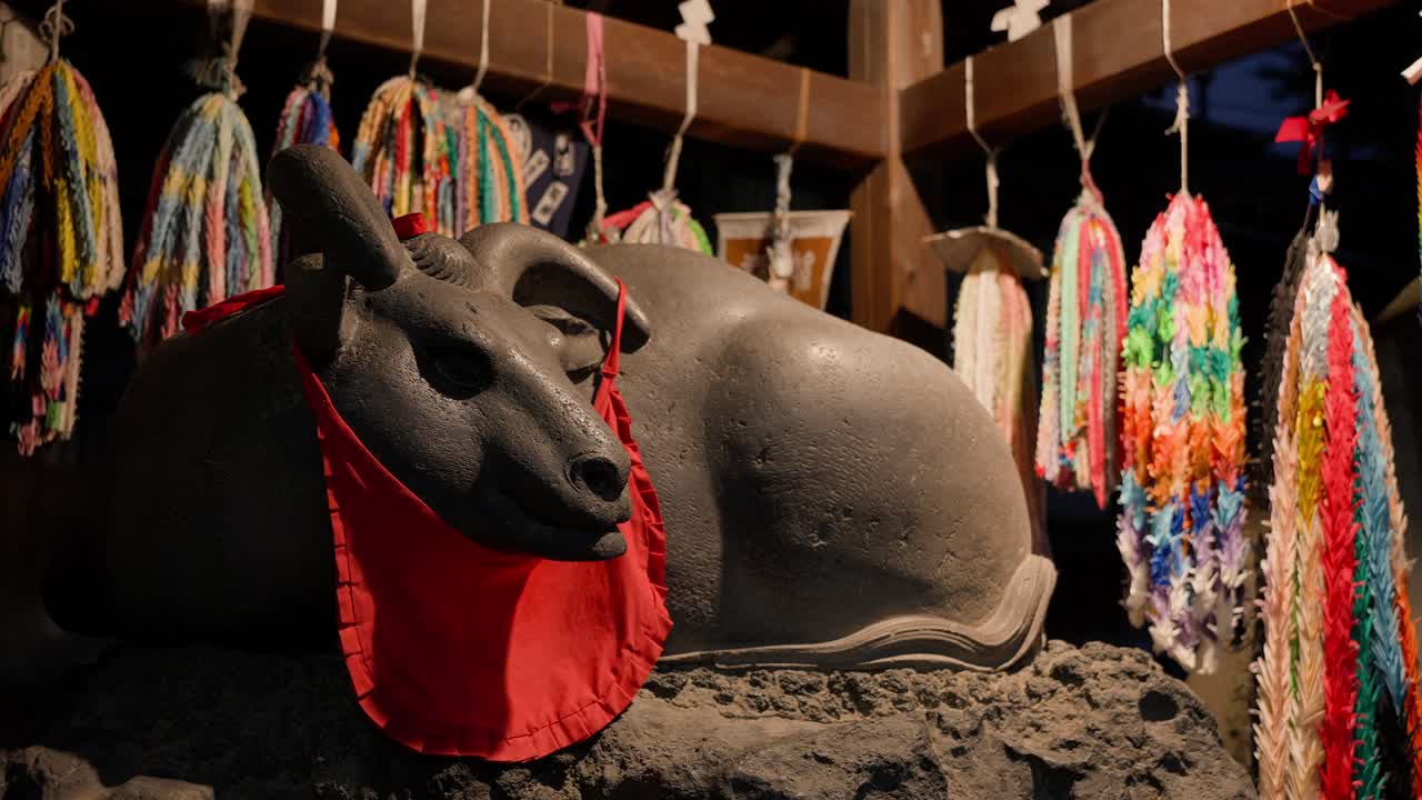 A stone ox statue with a red cloth and senbazuru decorations at Ushijima Shrine