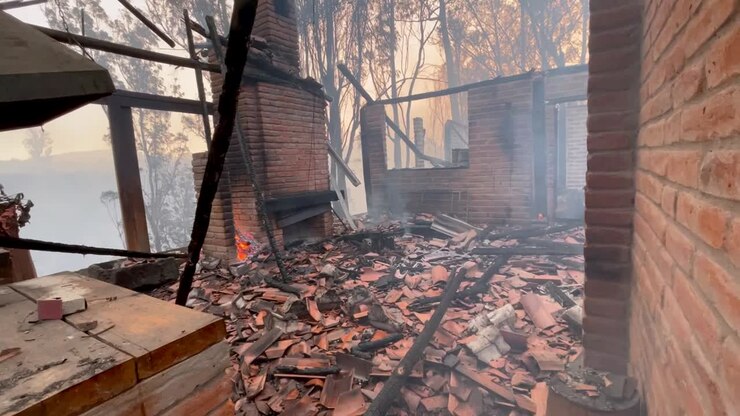 Sale humo de los escombros, la madera quemada y las tejas de una casa que ha quedado reducida a cenizas por un incendio forestal