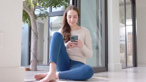 happy caucasian woman sitting on floor and using smartphone in slow motion