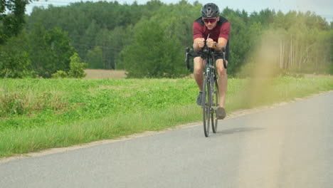 Professional-cyclist-sedulously-cycling-on-bike-in-summer-country-landscape,-fit-athlete-sport-workout-training-in-slow-motion---front-view-from-behind-swaying-grass