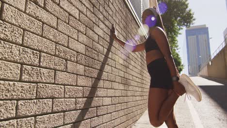 mujer afroamericana haciendo ejercicio al aire libre apoyándose en la pared y estirándose en la ciudad