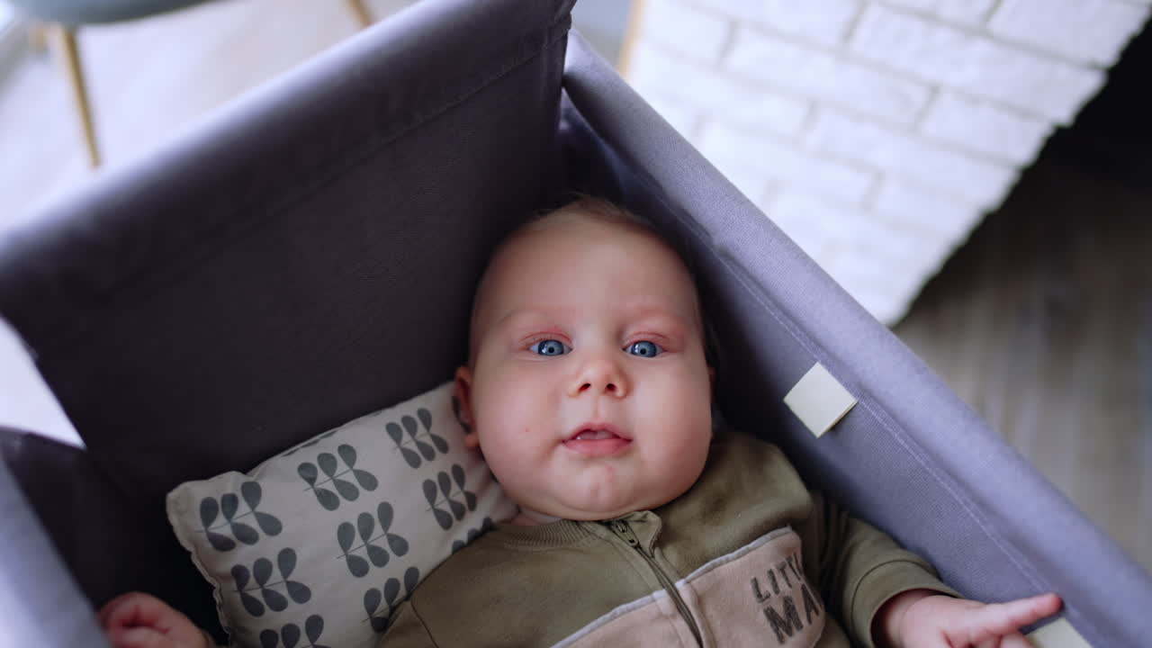Caucasian baby lies in the cradle waved by a parent. Stubborn kid doesn't want to fall asleep.