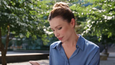 mujer de negocios tranquila escribiendo un mensaje en su teléfono inteligente sentada en un parque verde soleado de primer plano