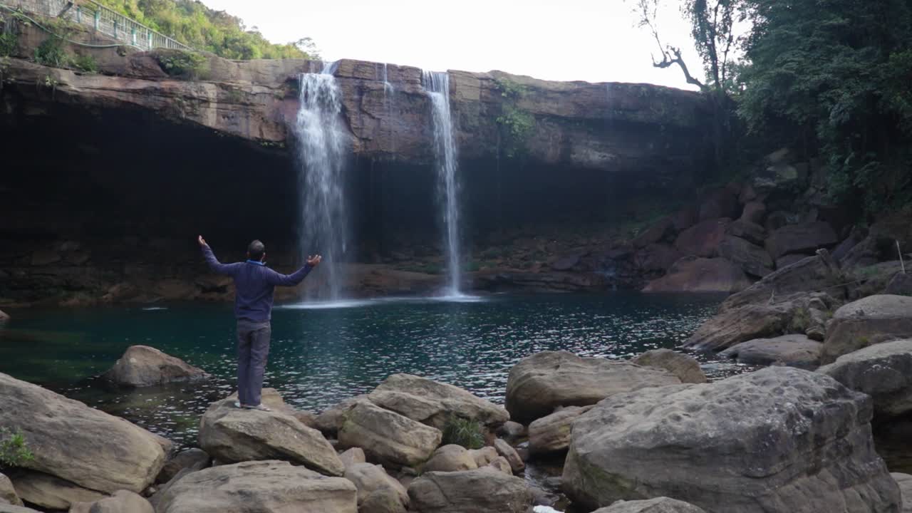 joven disfrutando de la cascada natural que cae desde la cima de la montaña en el video matutino tomado en la cascada krangsuri meghalaya india